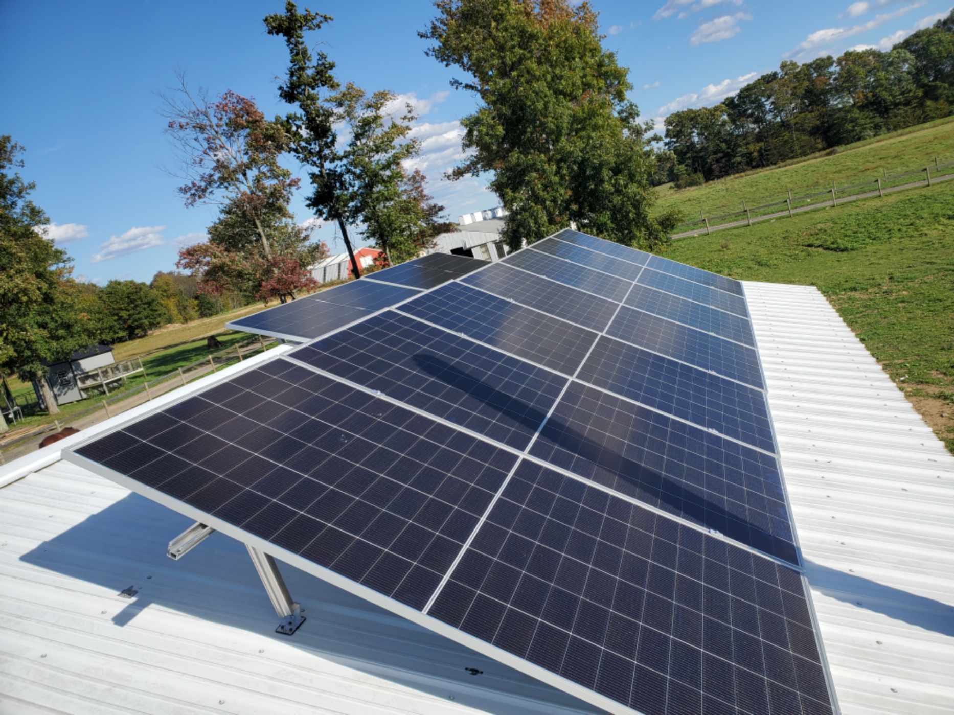 Solar panels on tilt racking above a white metal roof in rural Pennsylvania