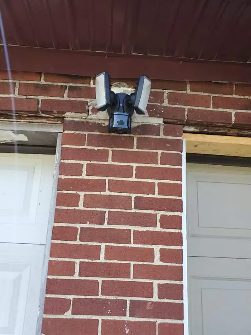 LED motion security light mounted on brick between garage doors
