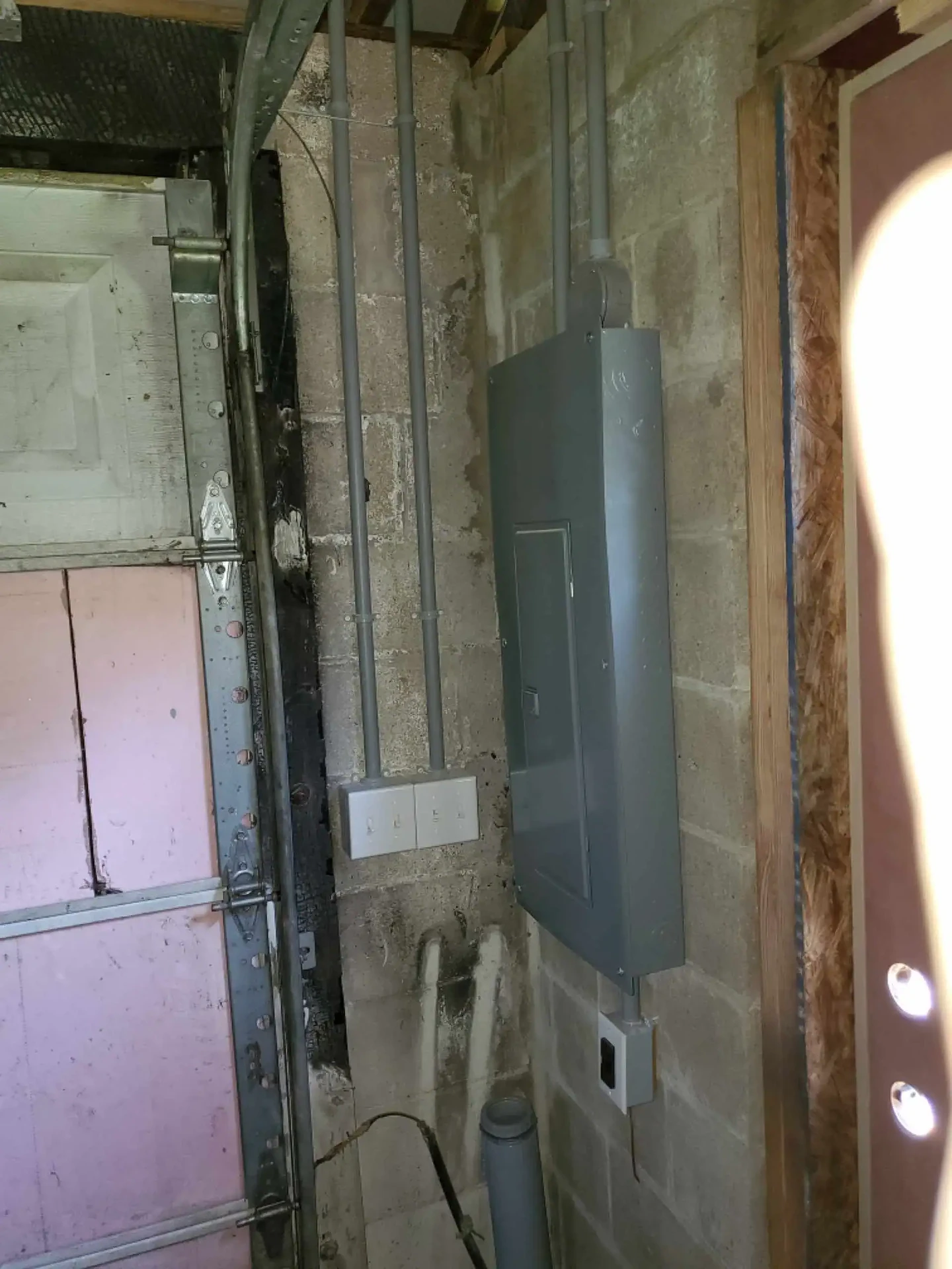 Garage electrical panel and switches with gray conduit on block wall